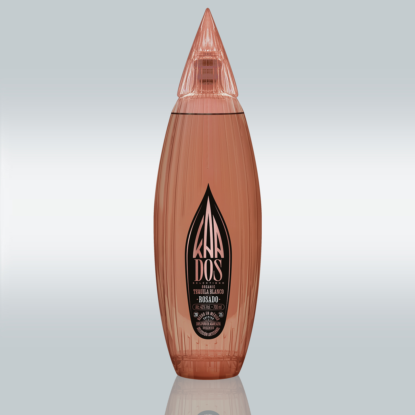 Studio shot of the KA DOS Rosado bottle centered on a gradient white-to-grey background. The sleek, vertically ribbed glass bottle in a warm rosé tone is shaped like an abstract agave leaf with a pointed, faceted cap. A large black KA DOS logo is prominently displayed on the front label, with details in gold and white text about the tequila’s organic origin, volume (700 ml), and alcohol content (40% vol).