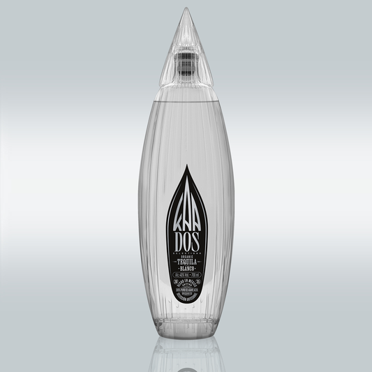 KA DOS Blanco bottle in sleek clear glass with vertical grooves and a sharp, faceted agave-leaf-shaped cap. Black-and-white front label features the KA DOS logo, “Organic Tequila Blanco”, 40% vol., 700 ml, and “100% Puro de Agave Azul”. Clean and modern design with artisanal detailing.